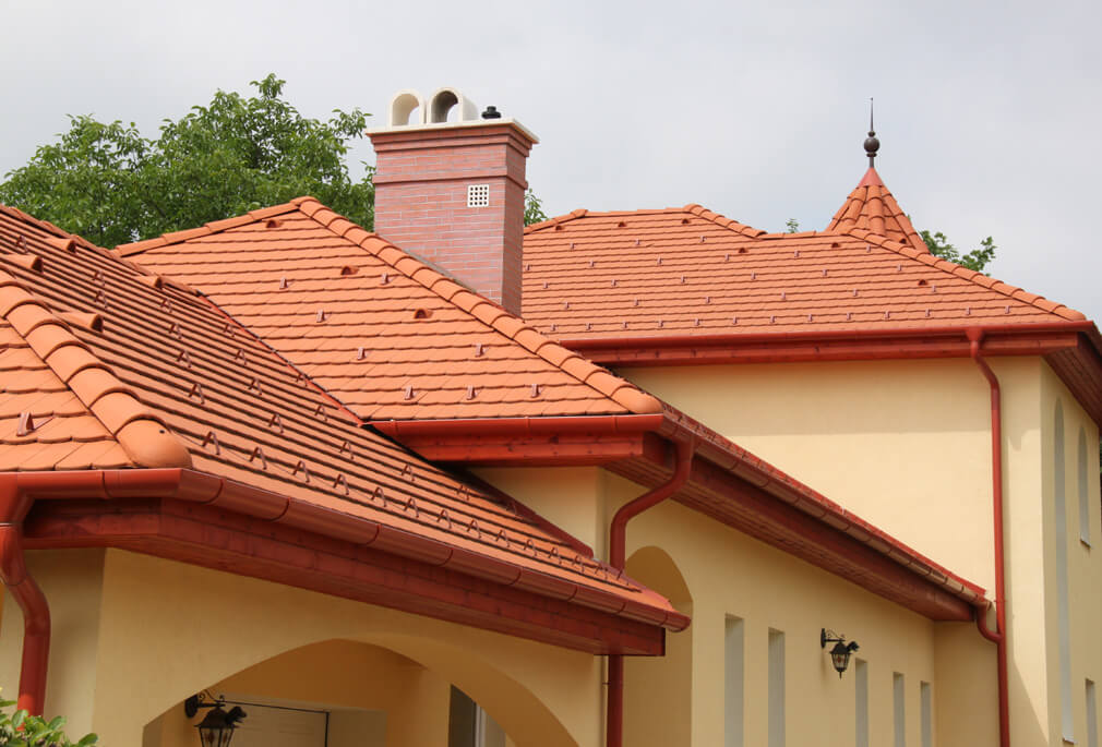 Detail červenej pálenej krytiny s komínom a kvalitnými odkvapmi